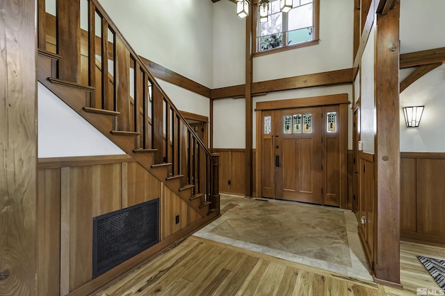 entryway with a towering ceiling, light hardwood / wood-style flooring, and wooden walls