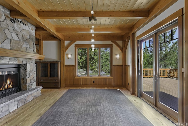 unfurnished living room featuring a fireplace, light wood-type flooring, beam ceiling, and wooden ceiling