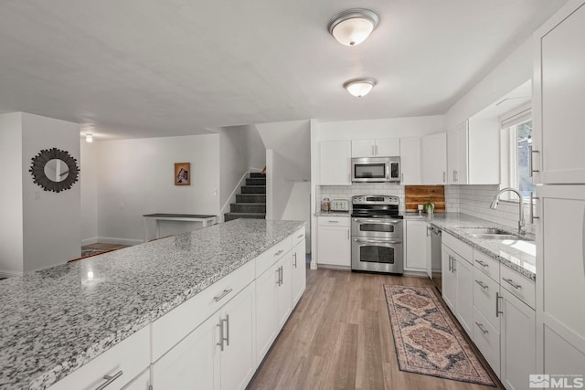 kitchen with white cabinetry, sink, light stone counters, and appliances with stainless steel finishes