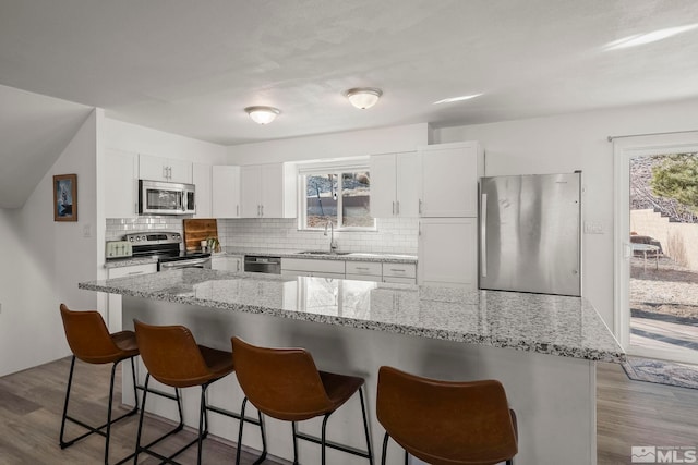 kitchen with appliances with stainless steel finishes, sink, a breakfast bar area, white cabinets, and light stone countertops