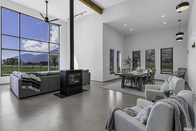 living room featuring beam ceiling, a towering ceiling, concrete flooring, a mountain view, and a wood stove