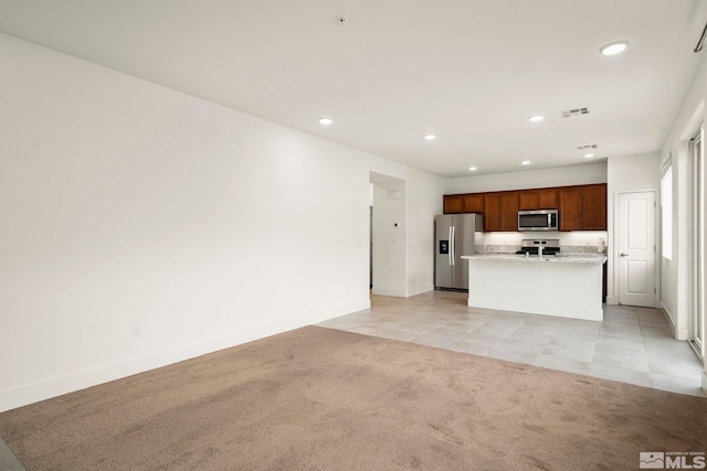 kitchen with light carpet, light stone countertops, stainless steel appliances, and a center island with sink