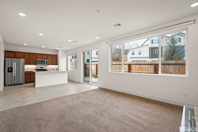 kitchen with stainless steel appliances, a kitchen island with sink, and light carpet