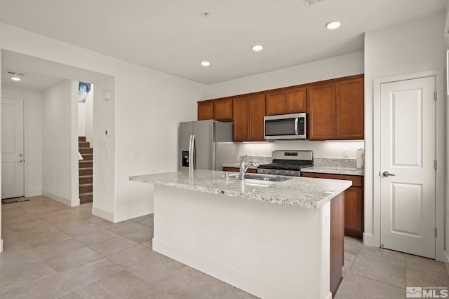 kitchen featuring sink, light tile patterned floors, stainless steel appliances, light stone countertops, and a center island with sink