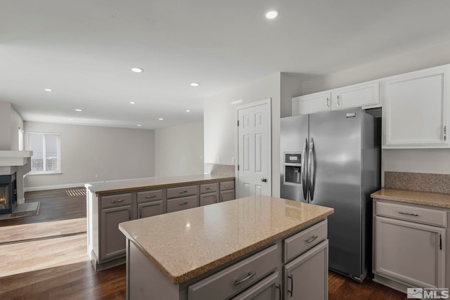 kitchen with stainless steel fridge, gray cabinetry, dark hardwood / wood-style floors, light stone counters, and a kitchen island