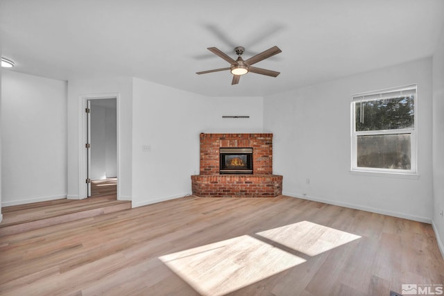 unfurnished living room featuring a brick fireplace, ceiling fan, and light hardwood / wood-style flooring