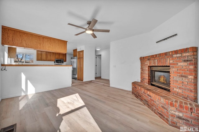 unfurnished living room with ceiling fan, a fireplace, and light wood-type flooring