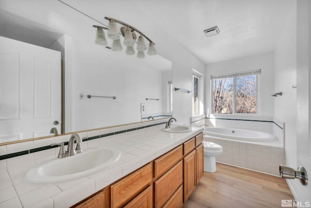 bathroom with wood-type flooring, vanity, toilet, tiled tub, and a textured ceiling