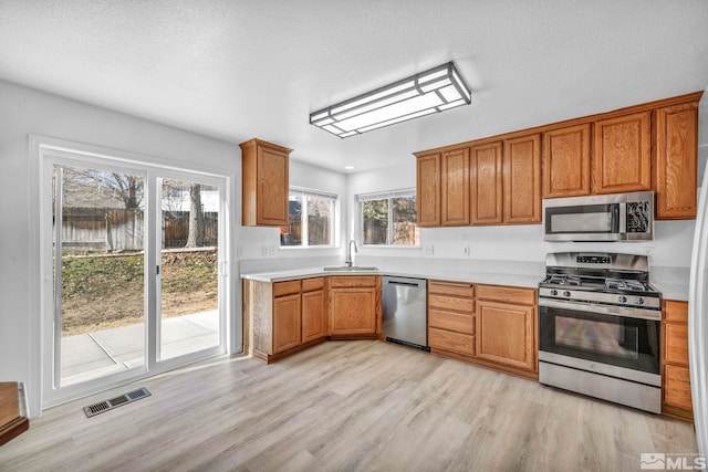 kitchen with appliances with stainless steel finishes, light hardwood / wood-style floors, sink, and a textured ceiling