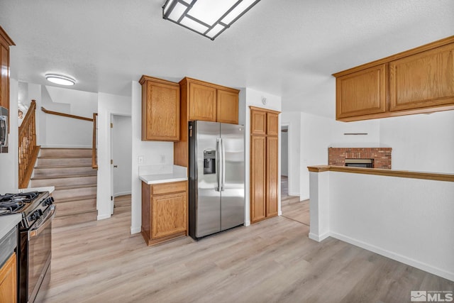 kitchen with a brick fireplace, light hardwood / wood-style flooring, stainless steel appliances, and a textured ceiling