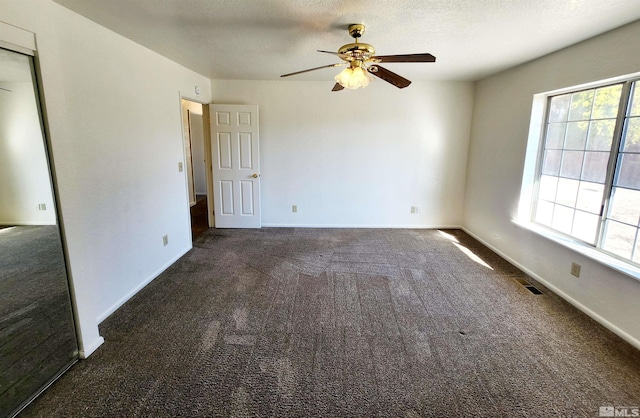 carpeted empty room featuring ceiling fan, a wealth of natural light, and a textured ceiling
