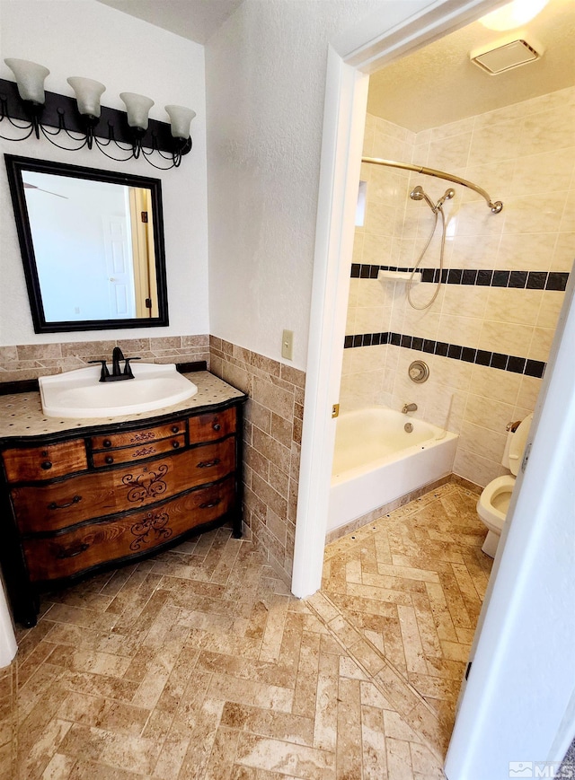 full bathroom with tile walls, vanity, tiled shower / bath combo, and toilet