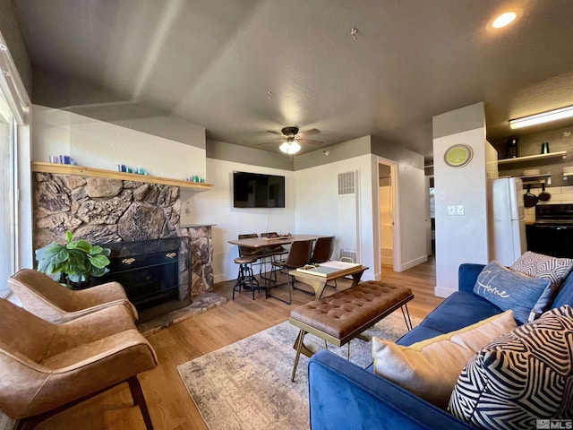 living room featuring a ceiling fan, light wood-type flooring, visible vents, and a stone fireplace