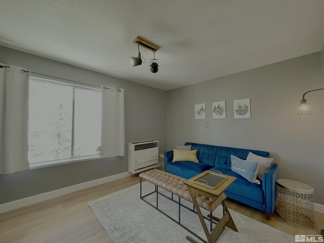 living room with heating unit, light wood-style flooring, and baseboards