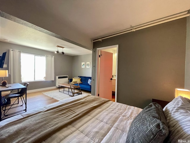 bedroom with heating unit, light wood-style floors, baseboards, and rail lighting