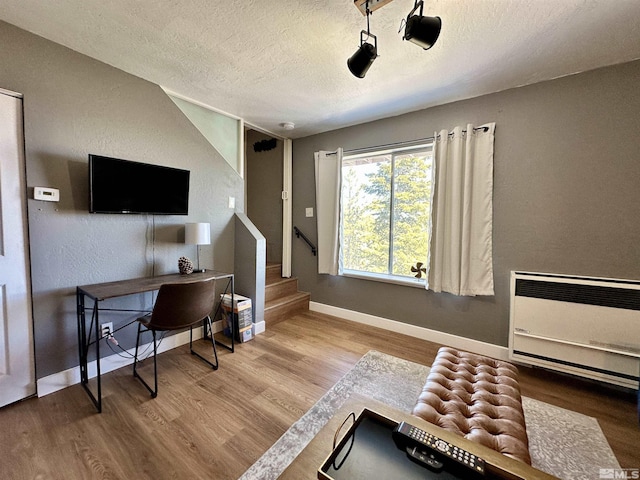 office space featuring baseboards, a textured wall, light wood-style flooring, heating unit, and a textured ceiling