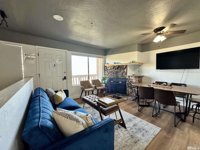 living room featuring baseboards, a textured ceiling, a ceiling fan, and wood finished floors