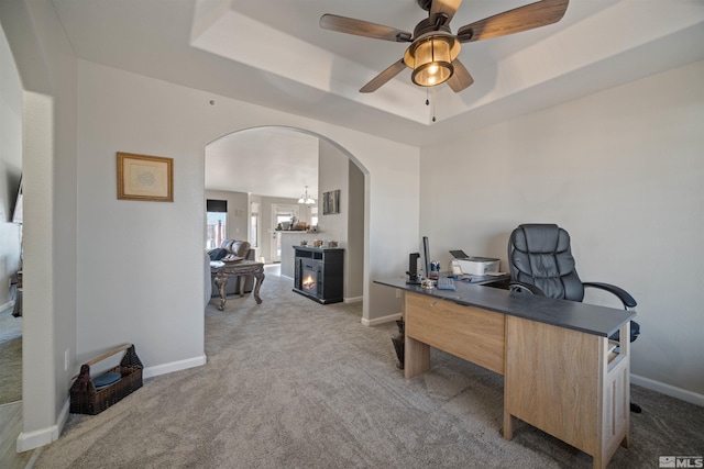 carpeted office space with a tray ceiling and ceiling fan