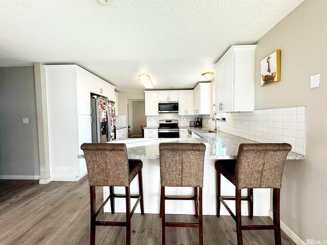 kitchen featuring sink, a breakfast bar area, white cabinets, kitchen peninsula, and stainless steel appliances