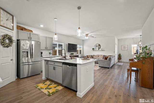 kitchen with sink, gray cabinets, appliances with stainless steel finishes, an island with sink, and decorative light fixtures