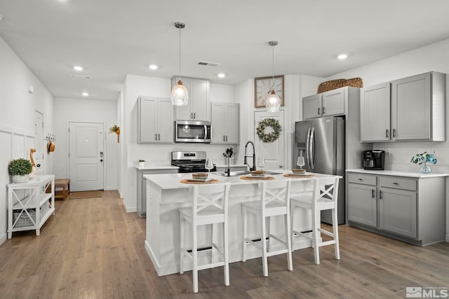 kitchen featuring gray cabinets, appliances with stainless steel finishes, a kitchen island with sink, a kitchen breakfast bar, and decorative light fixtures