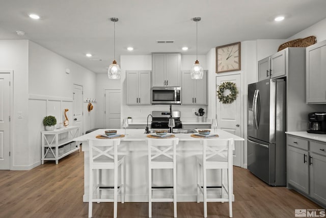 kitchen with pendant lighting, stainless steel appliances, a kitchen island with sink, and gray cabinetry