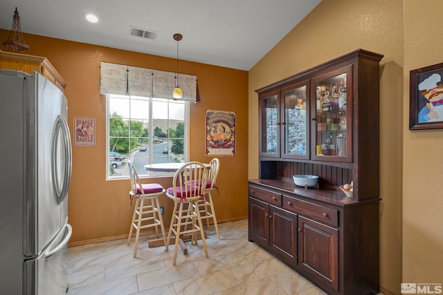 interior space featuring lofted ceiling, decorative light fixtures, stainless steel fridge, and dark brown cabinetry