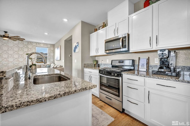 kitchen with stainless steel appliances, sink, white cabinets, and light stone counters