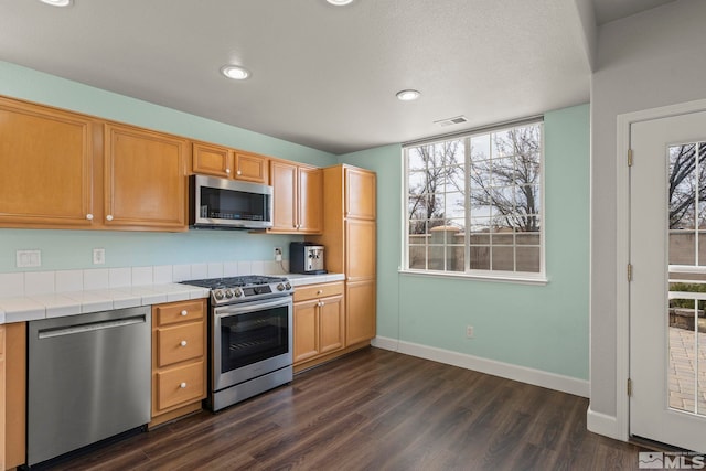 kitchen with appliances with stainless steel finishes, dark wood-type flooring, and tile countertops