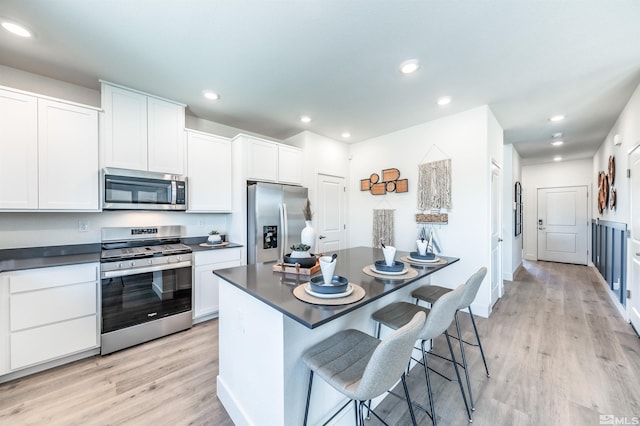 kitchen with appliances with stainless steel finishes, a breakfast bar area, white cabinets, and light hardwood / wood-style flooring