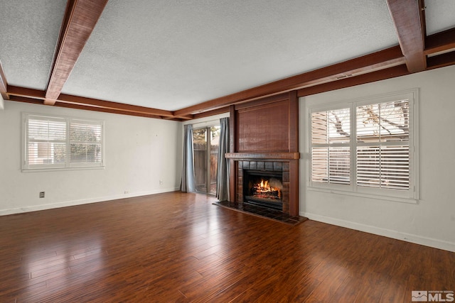 unfurnished living room with beamed ceiling, a fireplace, dark hardwood / wood-style flooring, and a wealth of natural light