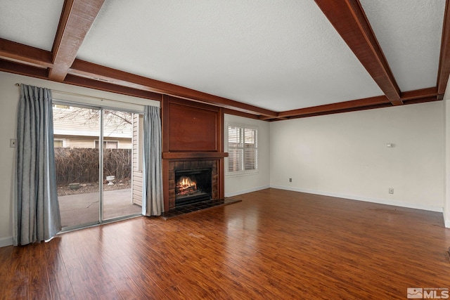 unfurnished living room featuring hardwood / wood-style flooring, a textured ceiling, a tile fireplace, and beamed ceiling