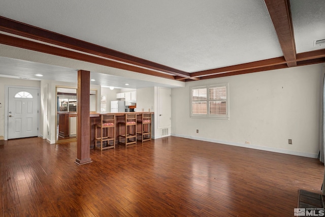 unfurnished living room featuring beam ceiling, dark hardwood / wood-style flooring, and a textured ceiling