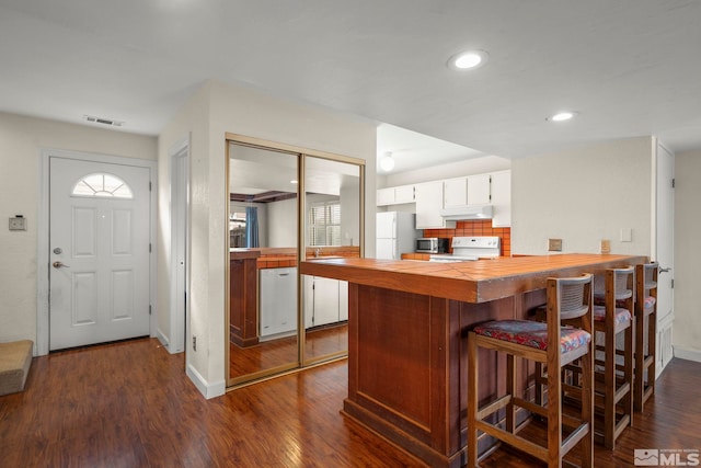 kitchen with white appliances, dark hardwood / wood-style floors, white cabinets, decorative backsplash, and kitchen peninsula