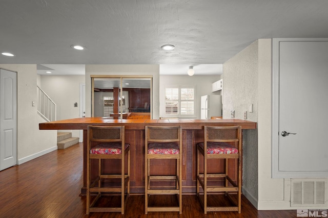 kitchen with white fridge, a kitchen bar, dark hardwood / wood-style flooring, and kitchen peninsula