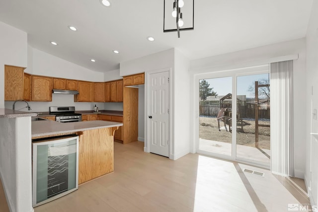 kitchen with sink, wine cooler, hanging light fixtures, stainless steel range oven, and light wood-type flooring