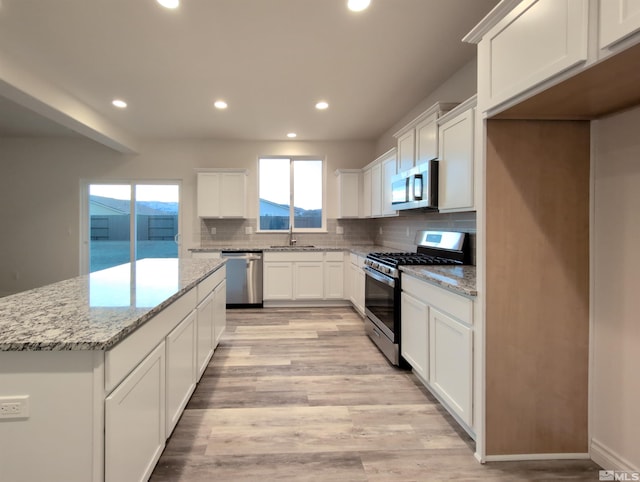 kitchen featuring a kitchen island, white cabinetry, sink, light stone counters, and stainless steel appliances