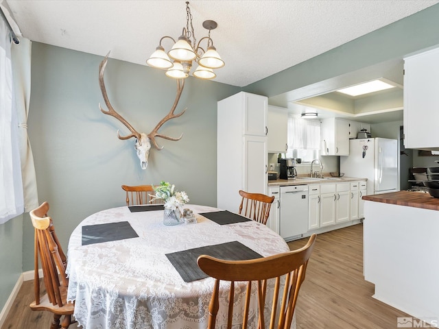 dining room featuring sink, a textured ceiling, a chandelier, and light wood-type flooring