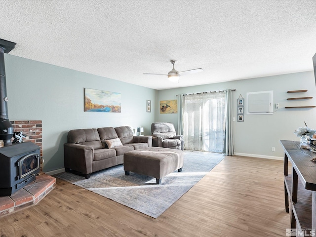 living room with ceiling fan, a wood stove, a textured ceiling, and light hardwood / wood-style floors