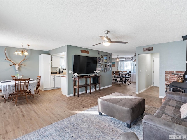 living room with ceiling fan with notable chandelier, light wood-type flooring, a textured ceiling, and a wood stove