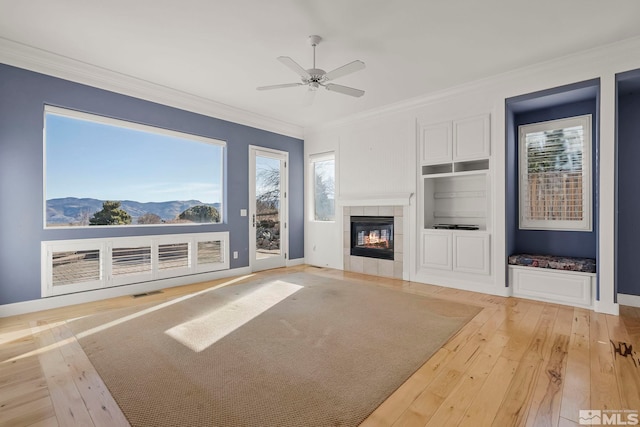 unfurnished living room with built in features, a fireplace, ornamental molding, a mountain view, and light hardwood / wood-style flooring