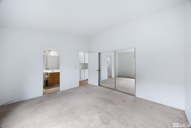 unfurnished bedroom with a closet, ensuite bath, and light carpet