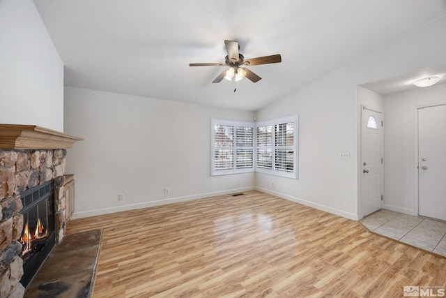 unfurnished living room featuring ceiling fan, lofted ceiling, a stone fireplace, and light hardwood / wood-style flooring