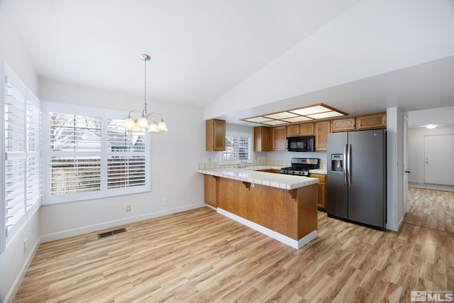 kitchen featuring lofted ceiling, a chandelier, kitchen peninsula, pendant lighting, and stainless steel appliances