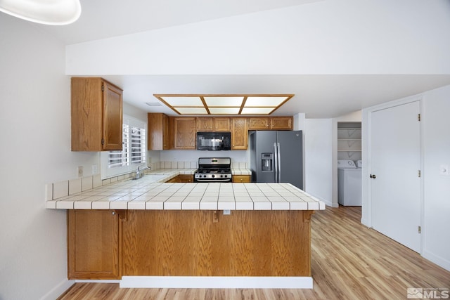 kitchen featuring sink, tile counters, kitchen peninsula, and appliances with stainless steel finishes