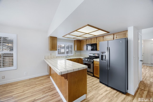 kitchen featuring stainless steel appliances, tile countertops, kitchen peninsula, and light hardwood / wood-style flooring