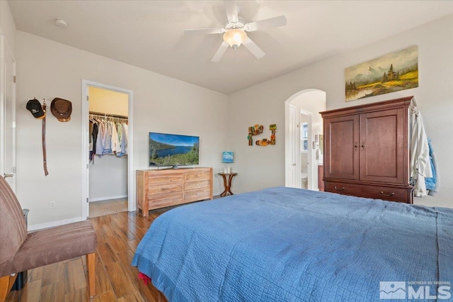 bedroom with dark hardwood / wood-style floors, connected bathroom, a walk in closet, ceiling fan, and a closet