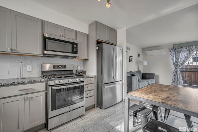 kitchen with gray cabinets, appliances with stainless steel finishes, tasteful backsplash, light stone counters, and a wall unit AC