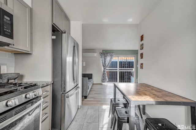 kitchen featuring appliances with stainless steel finishes, a wall mounted air conditioner, butcher block countertops, gray cabinetry, and decorative backsplash