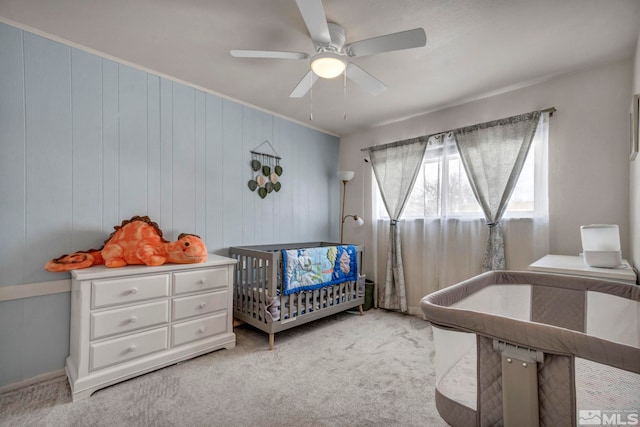 carpeted bedroom featuring a nursery area and ceiling fan